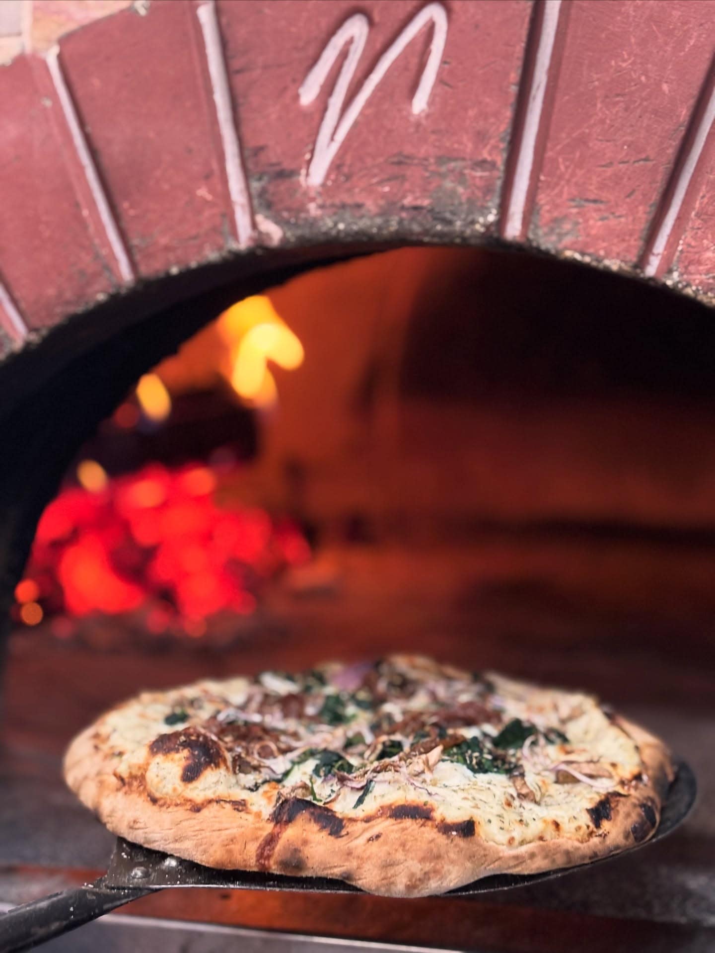 Wood-fired pizza on a peel in front of the glowing oven at Margherita Pizza in Meridian